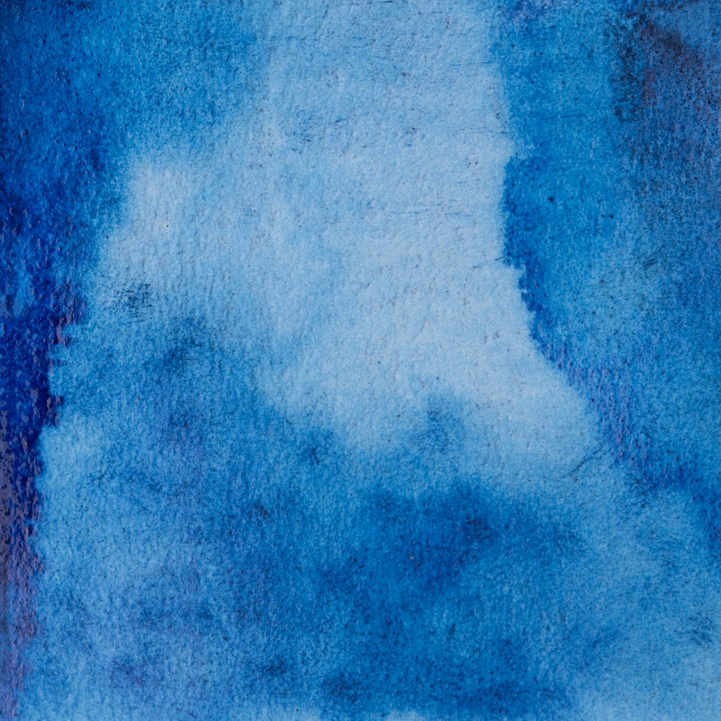 The image is a close-up of a textured blue surface, possibly a painting or a fabric. The color is predominantly blue, with some white and black accents visible. The surface appears to be textured, giving it a rough, uneven appearance. There are no discernible objects or actions depicted in the image, and the overall composition is simple and minimalistic.