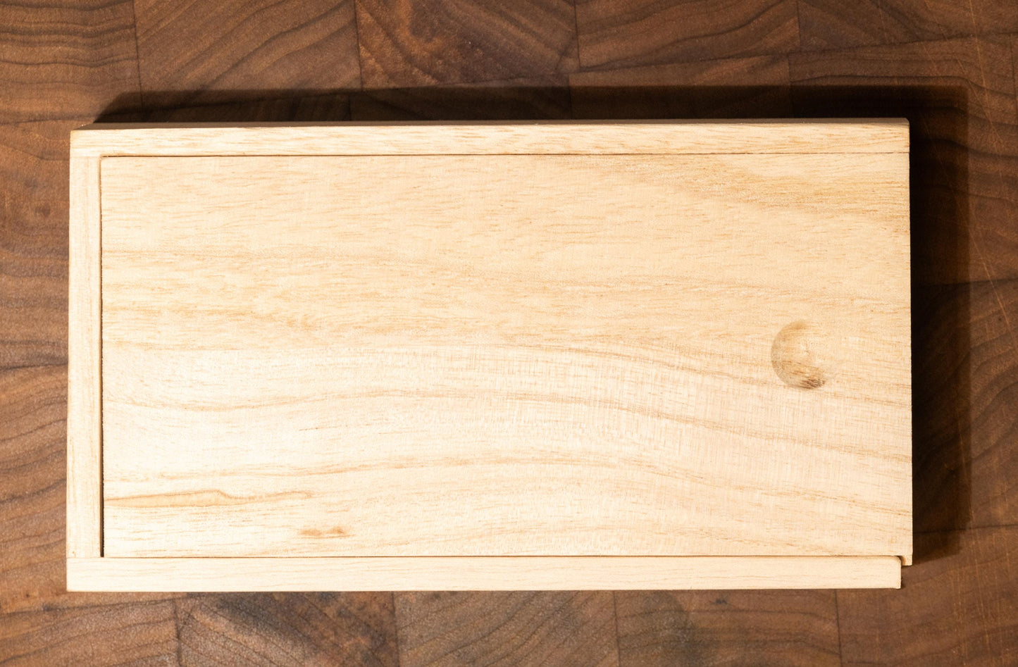 The wooden gift box closed and displayed on a black walnut board, with natural shredded paper peeking through the sides. Captured in soft lighting, this minimalistic image highlights the rustic beauty and gift-ready presentation of this premium handmade pigment set for artists and collectors.