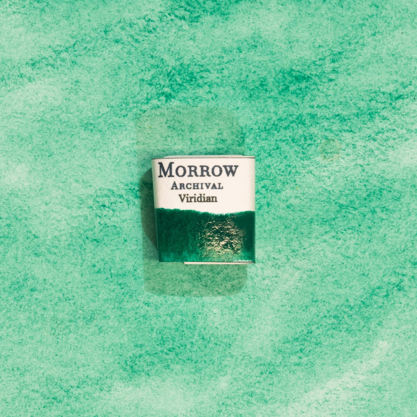 Handmade Viridian Green natural watercolor paint half pan resting on a textured watercolor painting. Crafted from pure single-pigment hydrated chromium oxide, this cool, vibrant green offers excellent transparency and smooth granulation, perfect for botanical illustration, landscape painting, and fine art. An ideal eco-friendly gift for watercolor artists and collectors seeking small-batch, archival-quality, all-natural handmade pigments rooted in historical tradition.