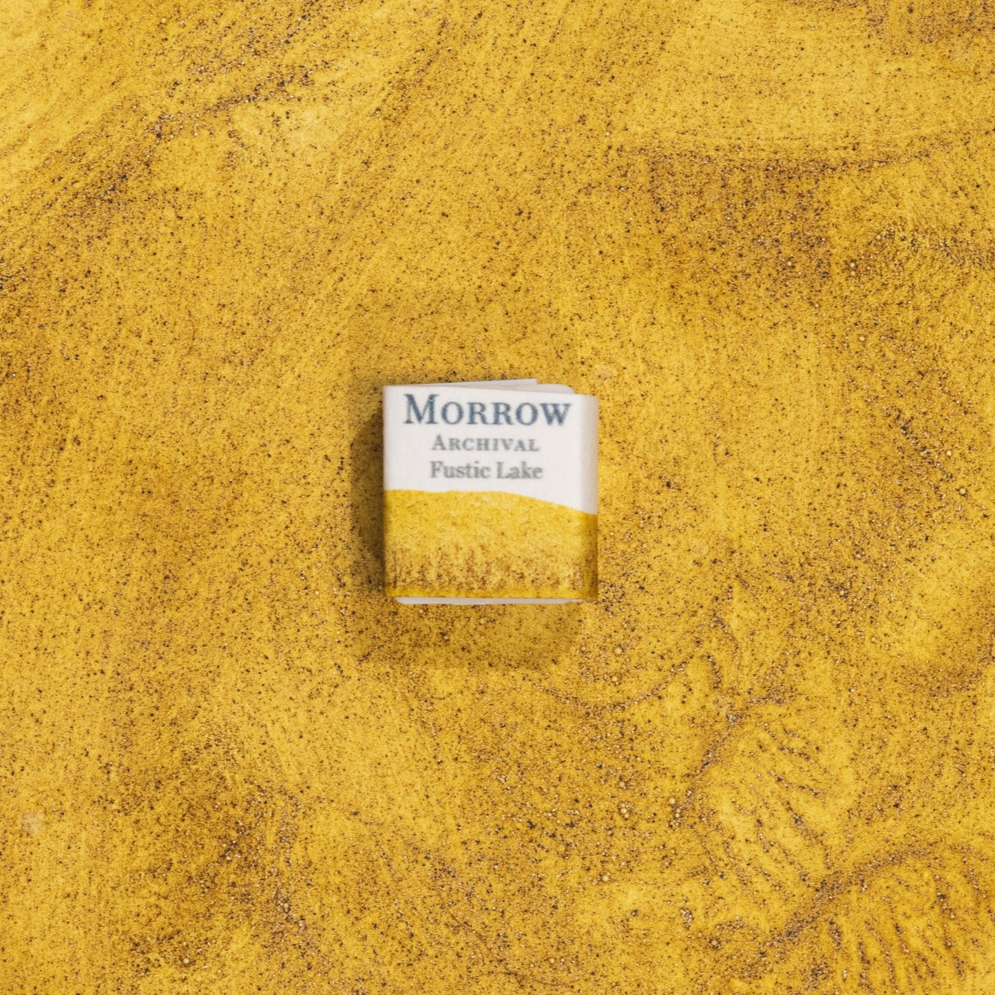Handmade Fustic Lake Deep Yellow natural watercolor paint half pan shown on a textured watercolor painting. Crafted from pure single-pigment fustic wood extract, this rich golden yellow offers warm transparency and soft granulation, perfect for botanical painting, historical illustration, and naturalist art. A beautiful eco-friendly gift for watercolor artists and collectors seeking small-batch, archival-quality, all-natural handmade pigments with a deep historical legacy.
