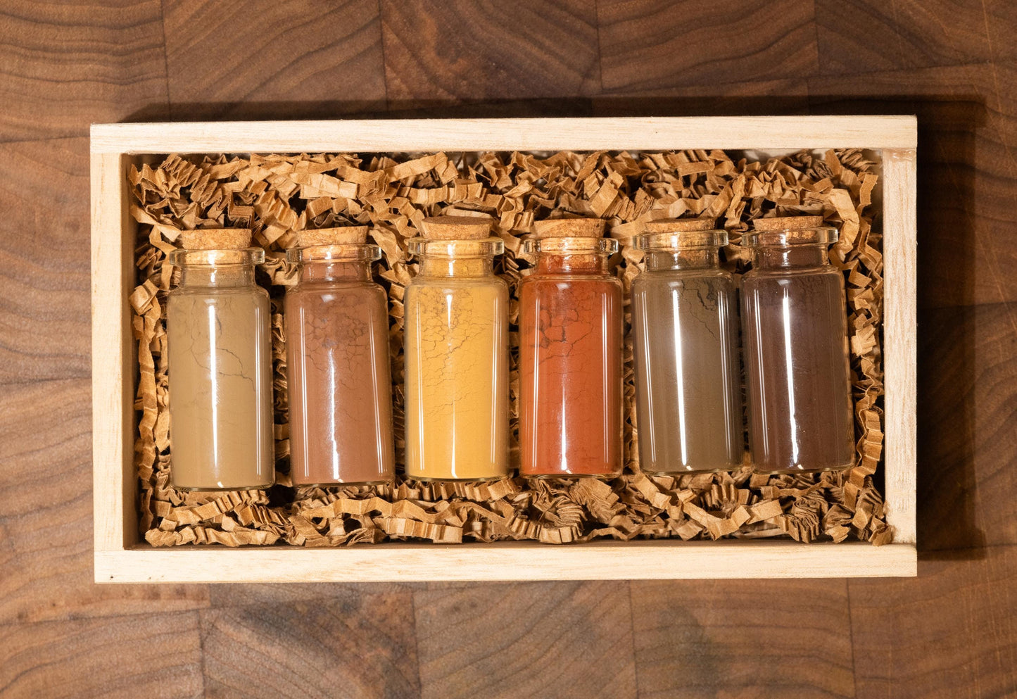 Set of 6 all natural ochre earth pigments in 1oz glass bottles with corks, nestled in shredded recycled kraft paper inside a handcrafted wooden gift box. Resting on a dark walnut wood board with soft, moody lighting, this all-natural artist gift set is ideal for birthdays, holidays, or creative milestones. Each bottle contains rich earth pigments in tones from golden yellow to deep green and warm brown as well as red and orange and are archival quality and lightfast for painting.