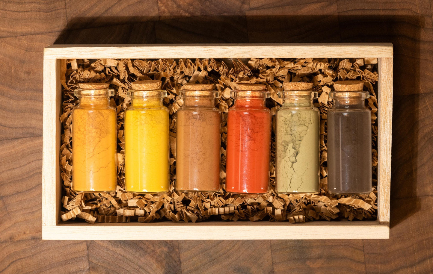 Set of 6 all natural ochre earth pigments in 1oz glass bottles with corks, nestled in shredded recycled kraft paper inside a handcrafted wooden gift box. Resting on a dark walnut wood board with soft, moody lighting, this all-natural artist gift set is ideal for birthdays, holidays, or creative milestones. Each bottle contains rich earth pigments in tones from golden yellow to deep green and warm brown as well as red and orange and are archival quality and lightfast for painting.