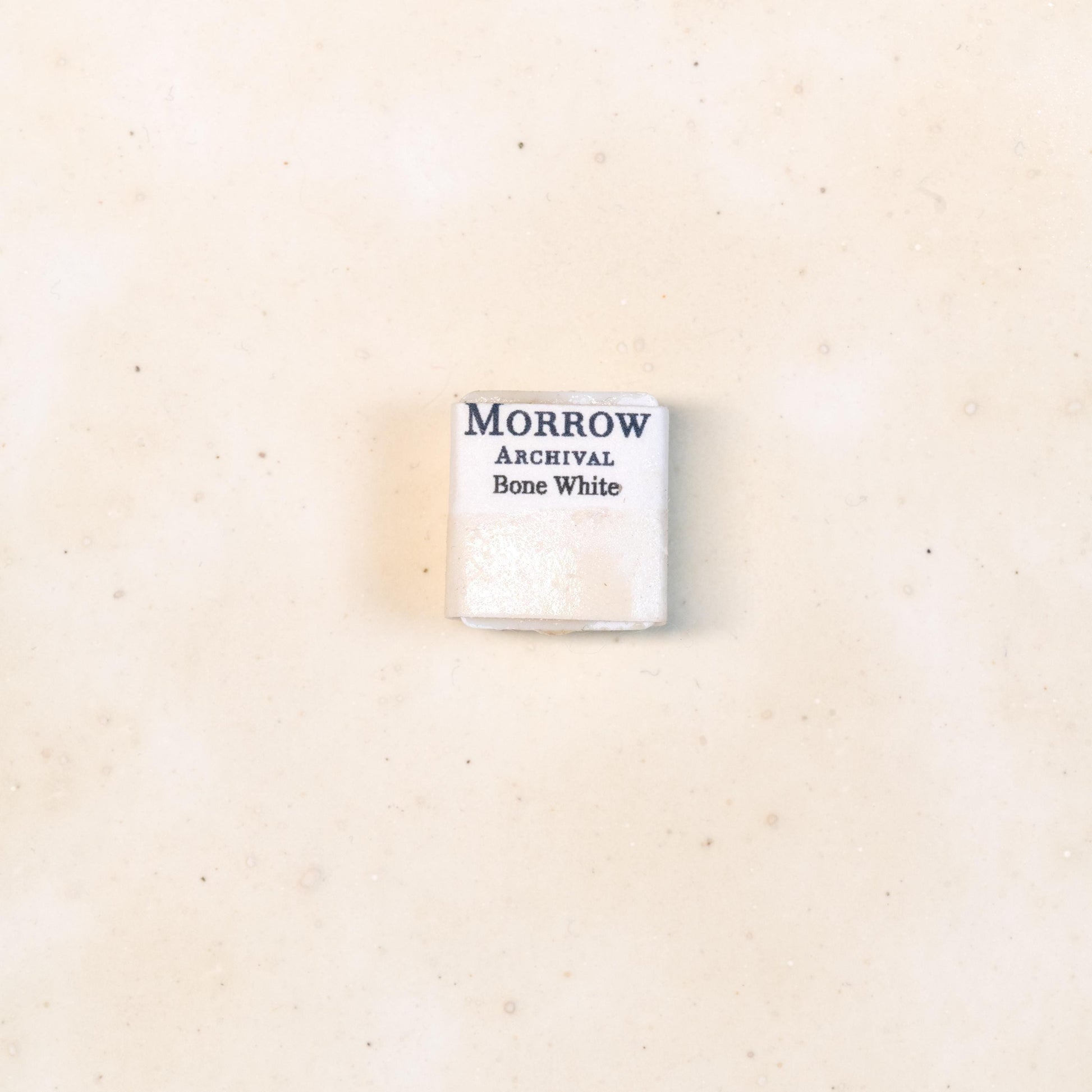 Close-up image of a half pan of Bone White handmade watercolor paint, featuring a soft, ivory-white hue with a smooth, semi-opaque finish. The pan rests on a neutral background, highlighting the pigment‚Äôs natural bone origin and artisanal craftsmanship. Ideal for artists seeking a warm, historic off-white for muted palettes and classical work.