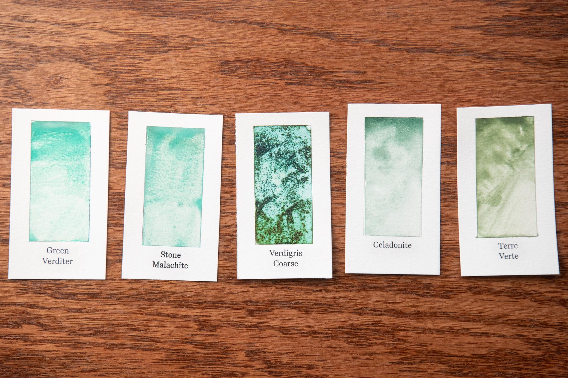 five white cards with different shades of green paint, each labeled with a different type of green paint.