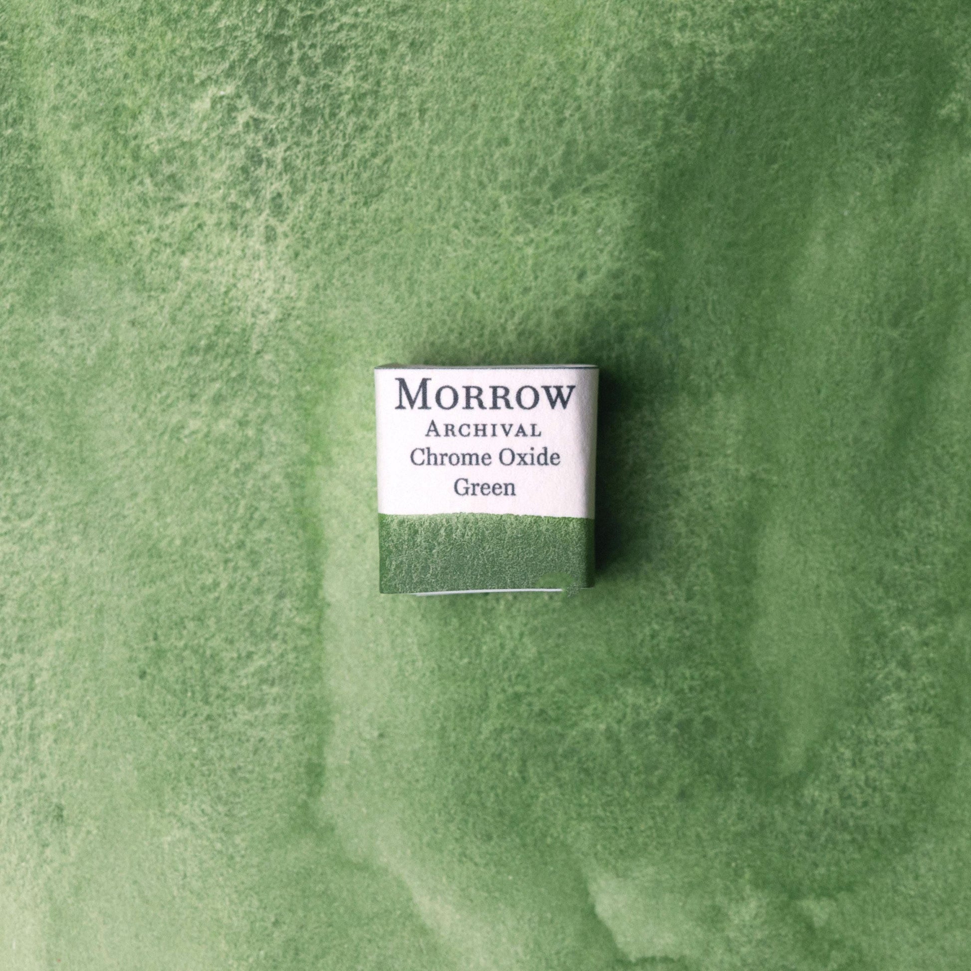 Handmade Chrome Green natural watercolor paint half pan shown on a textured watercolor painting. Crafted from pure single-pigment chromium oxide, this deep, opaque green offers strong coverage, smooth handling, and excellent lightfastness‚Äîperfect for botanical art, landscape painting, and historical illustration. A durable eco-friendly gift for watercolor artists and collectors seeking small-batch, archival-quality, all-natural handmade pigments rooted in traditional colormaking.