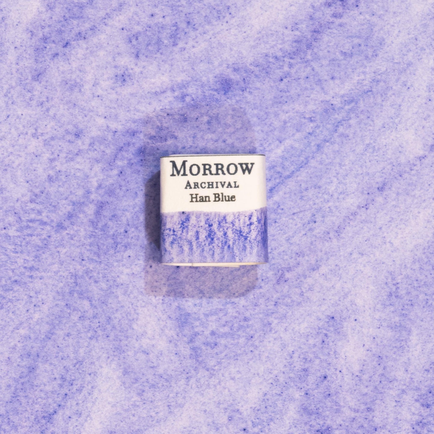 Handmade Han Blue natural watercolor paint half pan resting on a textured watercolor painting. Created from pure single-pigment synthetic blue based on ancient Chinese techniques, this luminous azure paint is ideal for fine art, historical painting, and detailed illustration. A perfect sustainable gift for watercolor artists, history enthusiasts, and collectors seeking archival-quality, small-batch, all-natural pigments with a rich cultural legacy.