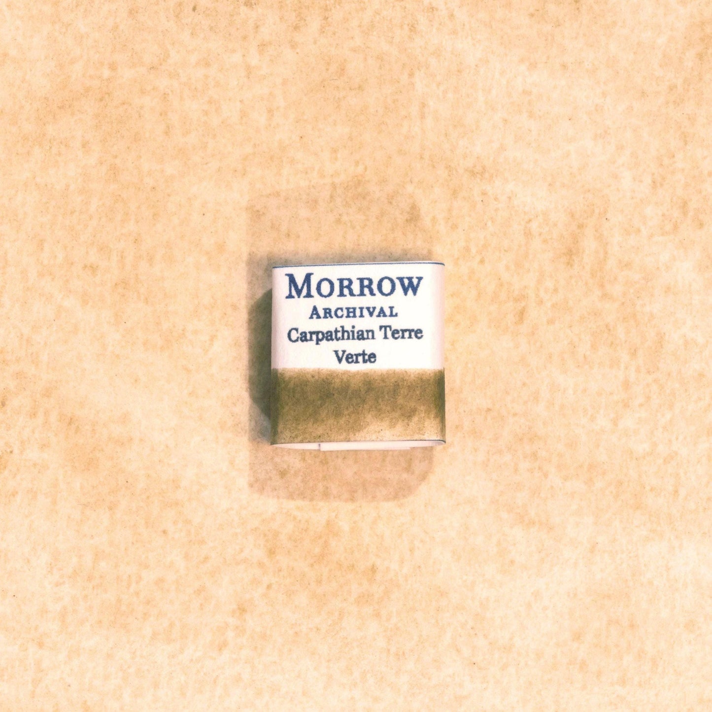 Handmade Carpathian Terre Verte natural watercolor paint half pan displayed on a textured watercolor painting. Crafted from pure single-pigment green earth sourced from the Carpathian Mountains, offering soft, muted green tones perfect for classical art, botanical work, and landscape painting. An ideal eco-friendly gift for artists, watercolorists, and historians who appreciate archival-quality, small-batch, all-natural pigments.