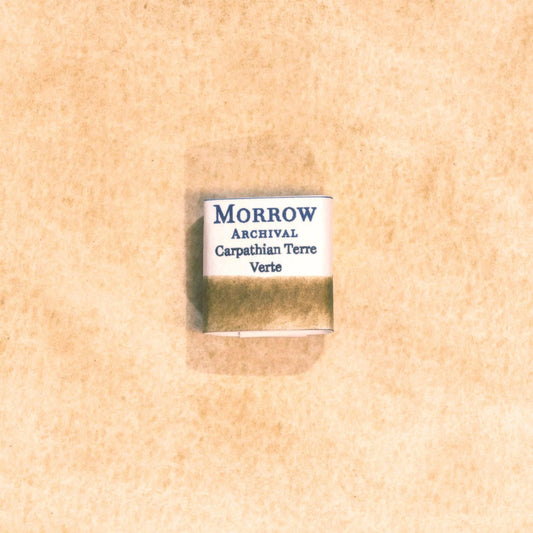 Handmade Carpathian Terre Verte natural watercolor paint half pan displayed on a textured watercolor painting. Crafted from pure single-pigment green earth sourced from the Carpathian Mountains, offering soft, muted green tones perfect for classical art, botanical work, and landscape painting. An ideal eco-friendly gift for artists, watercolorists, and historians who appreciate archival-quality, small-batch, all-natural pigments.