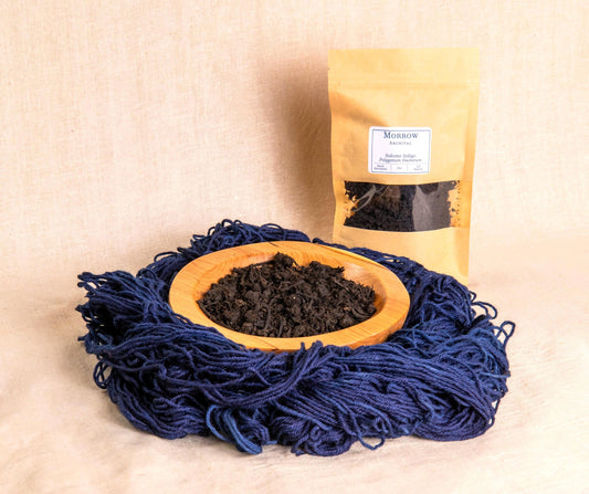 Sukumo Indigo Dye by Morrow Archival, shown as a rich, fermented blue leaf paste in a wooden bowl, with deep blue-dyed wool yarn and a labeled kraft pouch. Made from traditional Japanese Polygonum tinctorium leaves through compost fermentation, this historic indigo dye offers deep, enduring blues with unmatched richness. Perfect for natural vat dyeing, sashiko, shibori, and eco-conscious textile artists seeking authentic, artisan color.