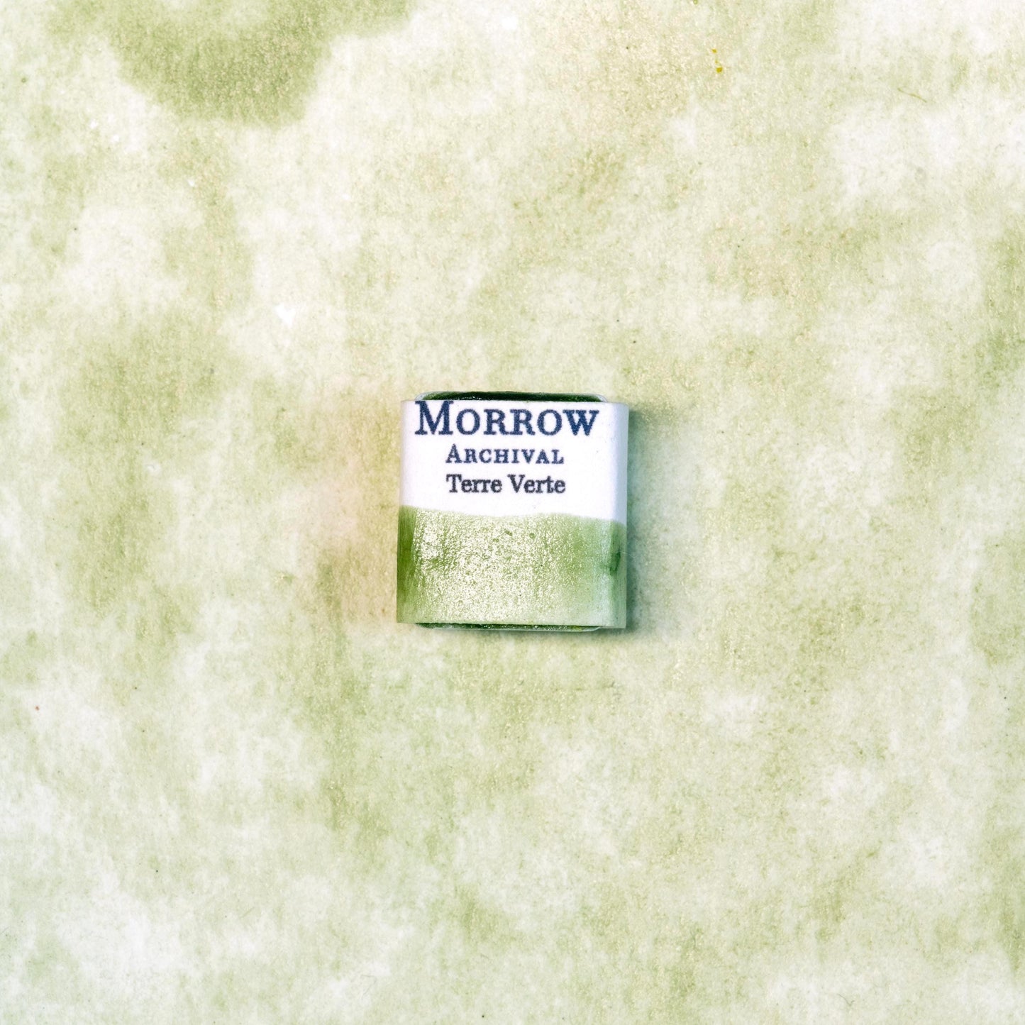 Close-up image of a half pan of Terre Verte handmade watercolor paint, showcasing a muted, cool green hue with a soft, natural matte texture. The paint is set against a neutral or rustic background, emphasizing its earthy, mineral origin and artisanal quality. Perfect for artists seeking a historically authentic, natural green pigment with gentle translucency and classic character.