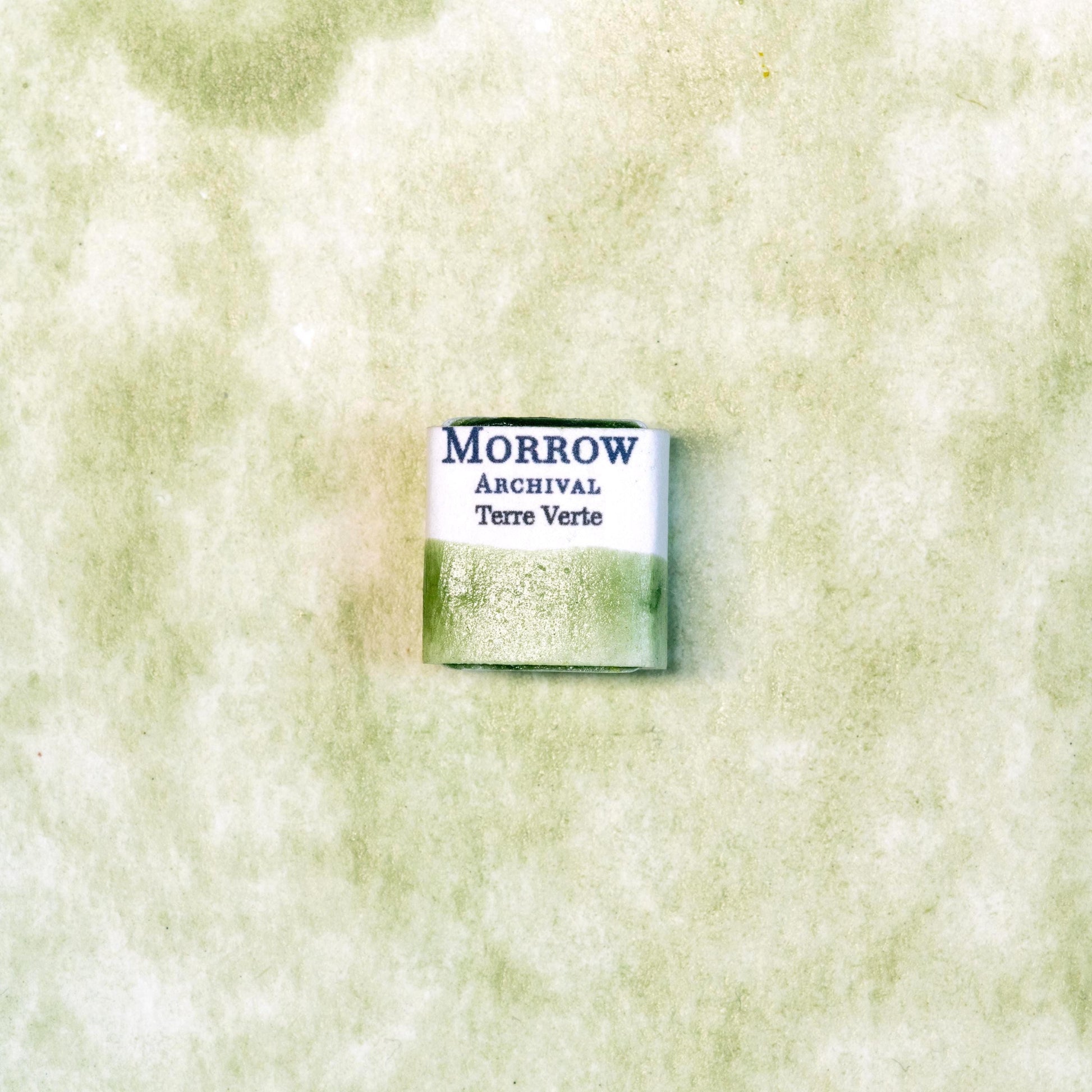 Close-up image of a half pan of Terre Verte handmade watercolor paint, showcasing a muted, cool green hue with a soft, natural matte texture. The paint is set against a neutral or rustic background, emphasizing its earthy, mineral origin and artisanal quality. Perfect for artists seeking a historically authentic, natural green pigment with gentle translucency and classic character.