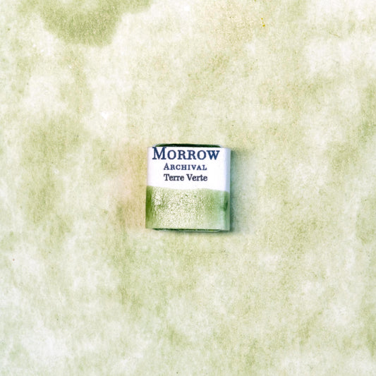 Close-up image of a half pan of Terre Verte handmade watercolor paint, showcasing a muted, cool green hue with a soft, natural matte texture. The paint is set against a neutral or rustic background, emphasizing its earthy, mineral origin and artisanal quality. Perfect for artists seeking a historically authentic, natural green pigment with gentle translucency and classic character.