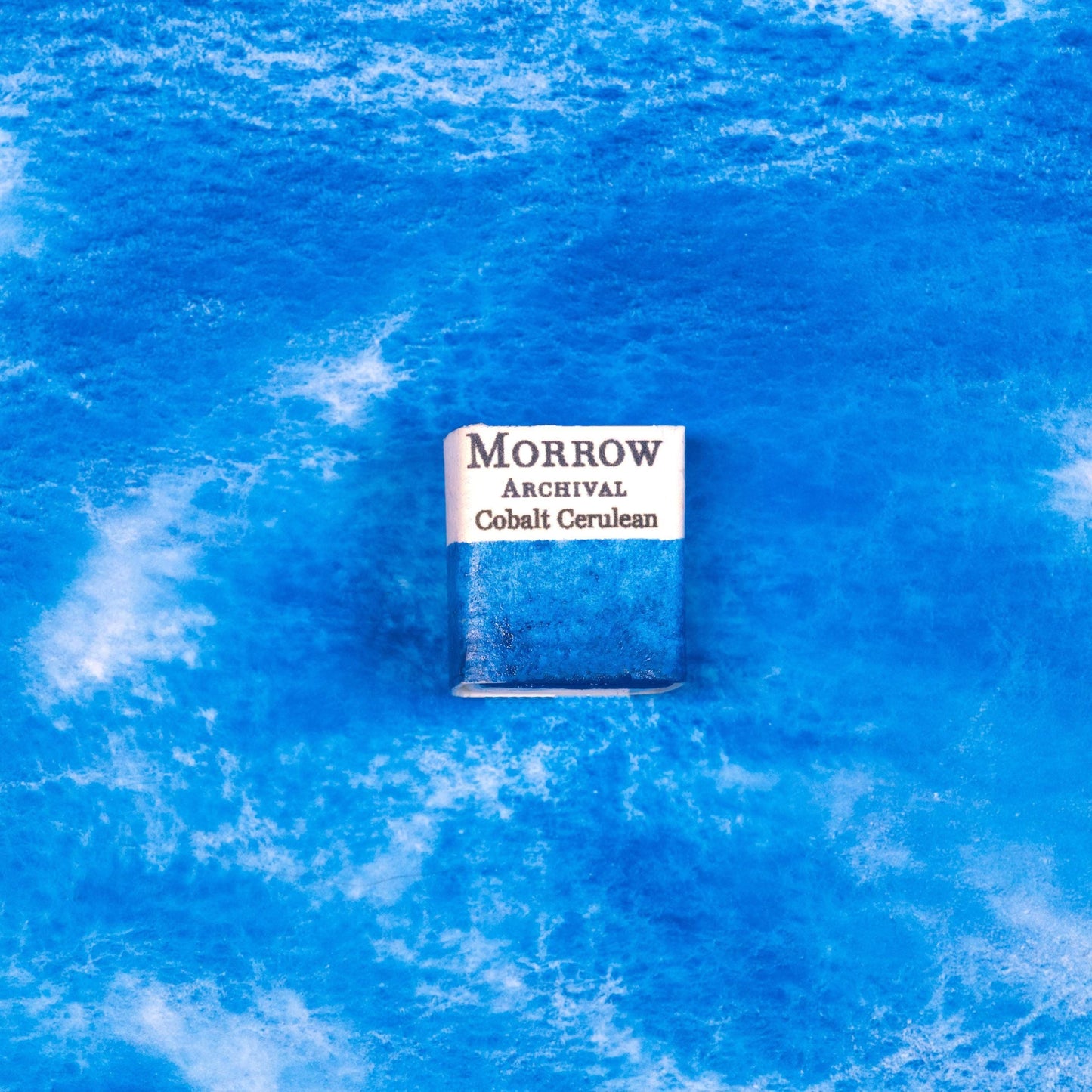 Close-up image of a half pan of Cobalt Cerulean handmade watercolor paint, featuring a soft, pastel blue with smooth granulation and a velvety, semi-opaque surface. The pan rests on a neutral background, emphasizing the paint‚Äôs mineral origin and artisanal craftsmanship. Ideal for artists seeking a serene, sky-like blue for landscapes and atmospheric effects.
