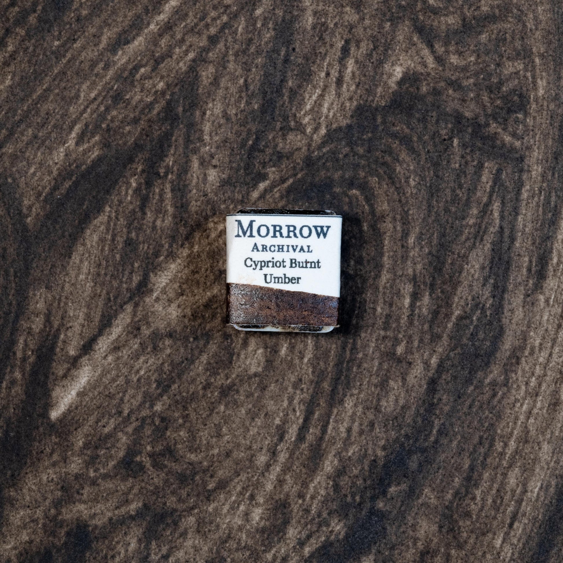 Close-up image of a half pan of Cypriot Burnt Ochre handmade watercolor paint, featuring a rich, reddish-brown hue with a soft matte surface and visible granulation. The pan rests on a neutral background, highlighting the pigment‚Äôs natural mineral origin and Mediterranean heritage. Ideal for artists seeking a warm, historic earth tone with depth and texture.