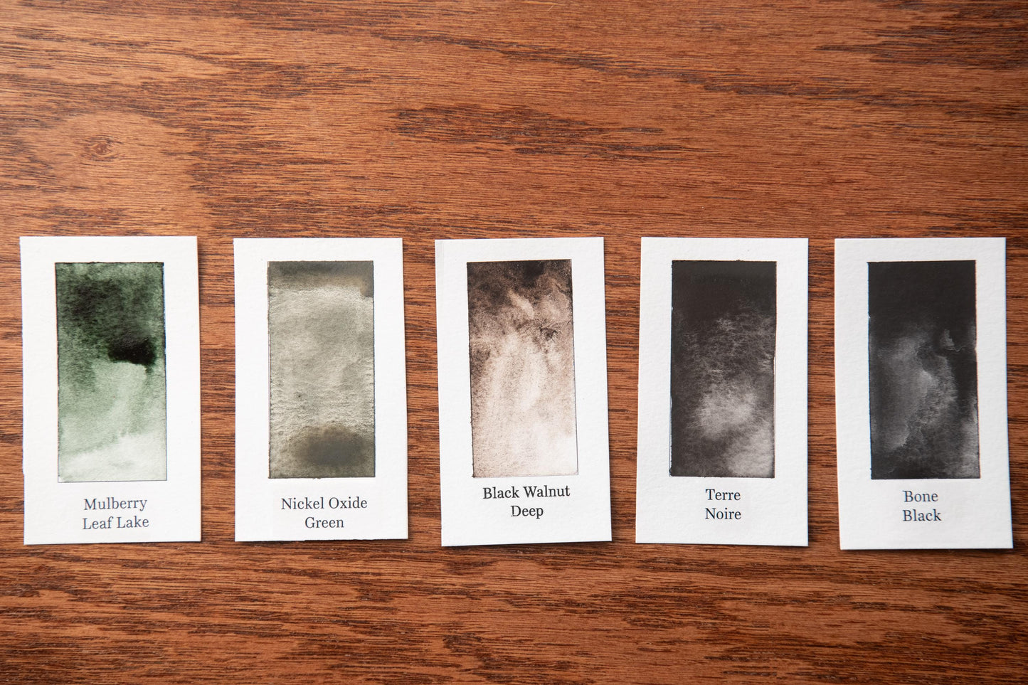 five watercolor paintings on a wooden surface, each with a different color and texture.