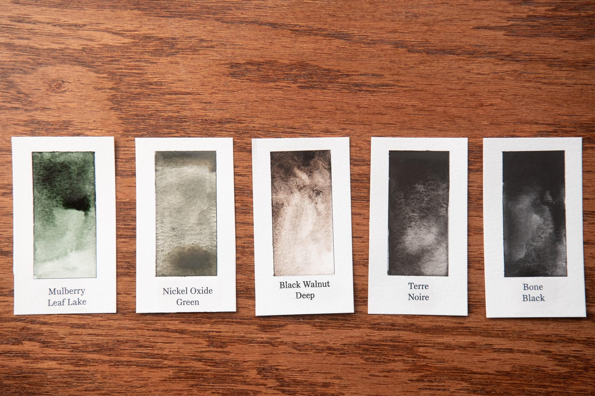 five watercolor paintings on a wooden surface, each with a different color and texture.