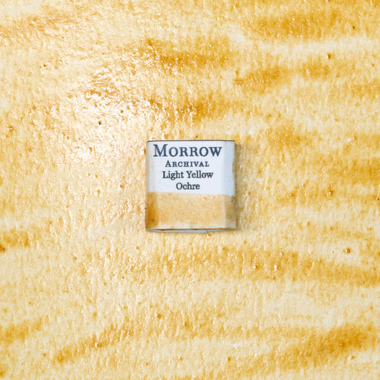 Close-up image of a half pan of Light Yellow Ochre handmade watercolor paint, showing a soft, warm golden-yellow color with a smooth, matte texture. The pan rests on a neutral-toned background, highlighting its natural earth origin and artisanal, small-batch craftsmanship. Ideal for artists seeking a timeless, light ochre pigment with historical significance and rich, natural tone.