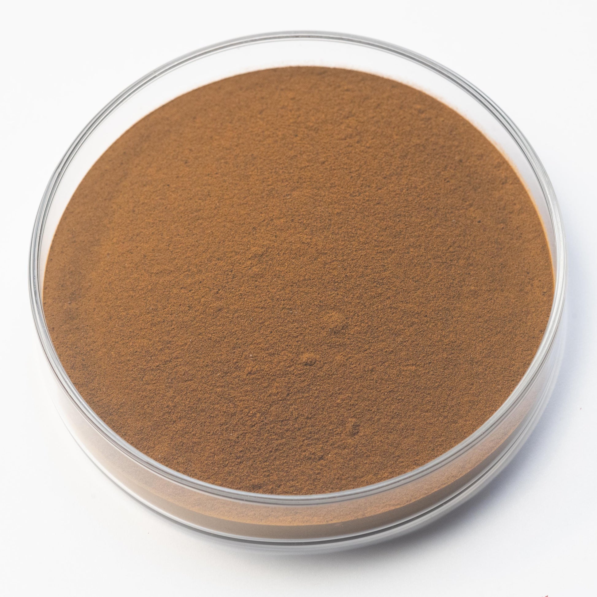 A clear glass petri dish contains Aloe Ferrox Pigment, a fine, light brown handmade botanical powder, displayed on a white background.