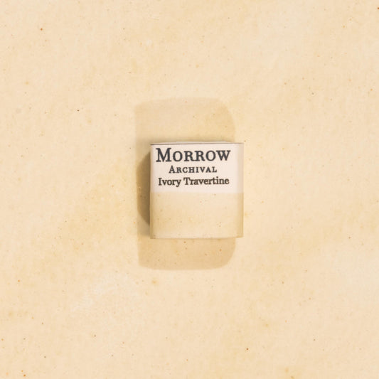 Handmade Ivory Travertine natural watercolor paint half pan resting on a textured watercolor painting. Made from pure single-pigment natural stone, this soft, warm off-white offers subtle granulation and delicate transparency, perfect for botanical painting, historical artwork, and fine art layering. A beautiful eco-friendly gift for watercolor artists and collectors seeking small-batch, archival-quality, all-natural handmade pigments inspired by ancient materials.