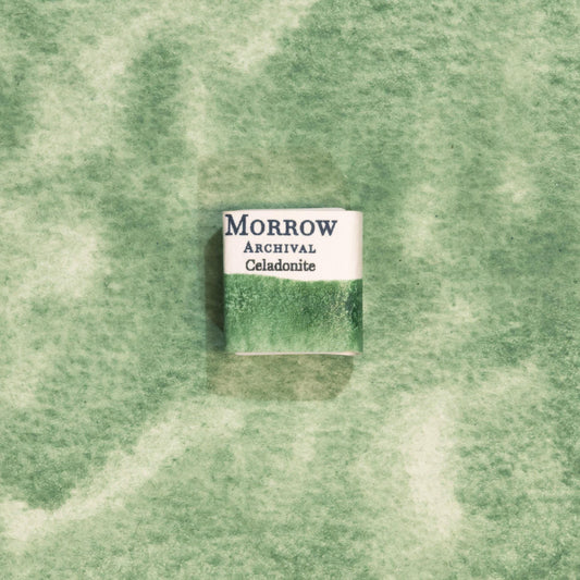 Handmade Celadonite Green Earth ochre natural watercolor paint half pan resting on a textured watercolor painting. Crafted from pure single-pigment celadonite mineral, this soft, muted green offers beautiful transparency and fine granulation, ideal for landscape painting, botanical illustration, and historical artwork. A perfect eco-friendly gift for watercolor artists and collectors seeking small-batch, archival-quality, all-natural handmade pigments with ancient roots.