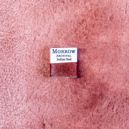 Close-up image of a half pan of Indian Red handmade watercolor paint, showing a dense, cool-toned brick red with a smooth matte surface and slight granulation. The pan is displayed on a neutral background, highlighting its natural mineral origin and artisanal craftsmanship. Ideal for artists seeking a historic, opaque red with depth and classical appeal.