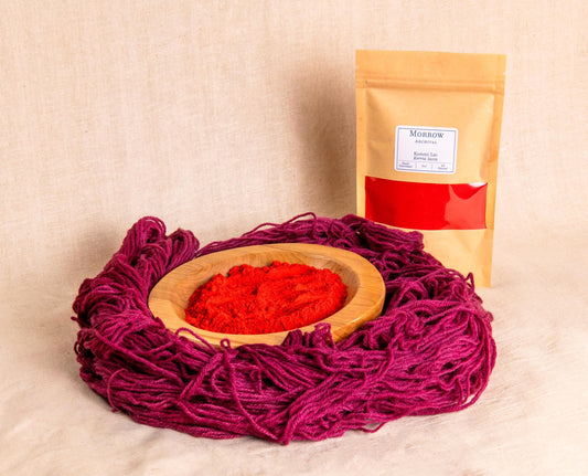Lac Dye by Morrow Archival, shown as a fine reddish powder in a wooden bowl with richly dyed crimson wool yarn and a labeled kraft pouch in the background. Sourced from secretions of the Kerria lacca insect, this historic natural dye has been used for centuries across Asia for deep pinks, purples, and reds. Ideal for natural textile dyeing, historic reproduction, and eco-friendly fiber arts using sustainable, artisan-crafted dyes.