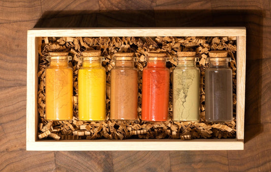 Set of 6 all natural ochre earth pigments in 1oz glass bottles with corks, nestled in shredded recycled kraft paper inside a handcrafted wooden gift box. Resting on a dark walnut wood board with soft, moody lighting, this all-natural artist gift set is ideal for birthdays, holidays, or creative milestones. Each bottle contains rich earth pigments in tones from golden yellow to deep green and warm brown as well as red and orange and are archival quality and lightfast for painting.