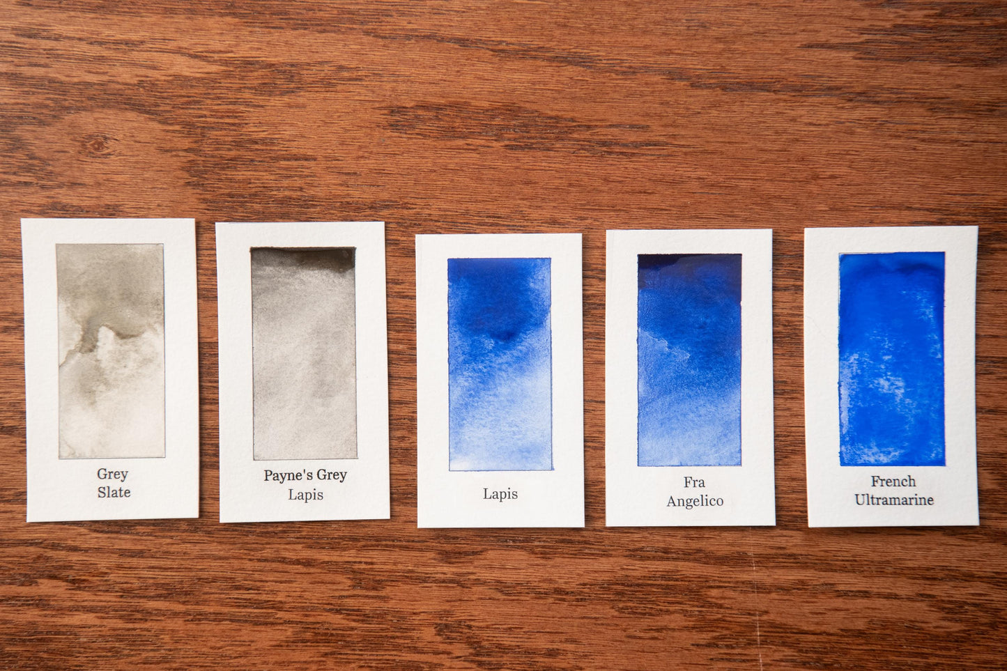 five watercolor paintings with different shades of grey, each labeled with the name of the artist.