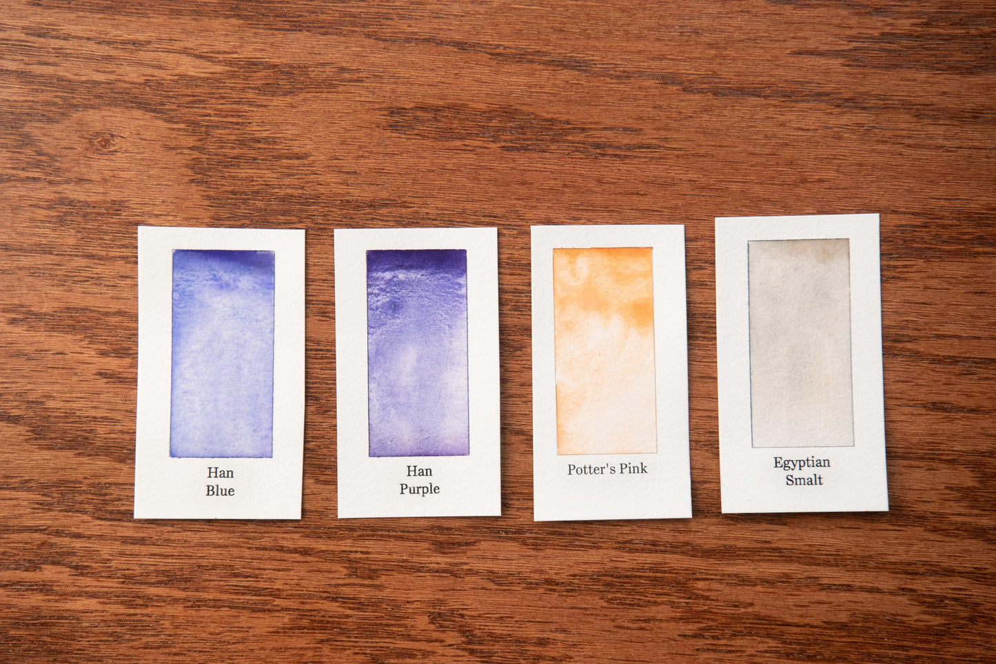 four small rectangular cards with different paint color swatches, arranged on a wooden surface.