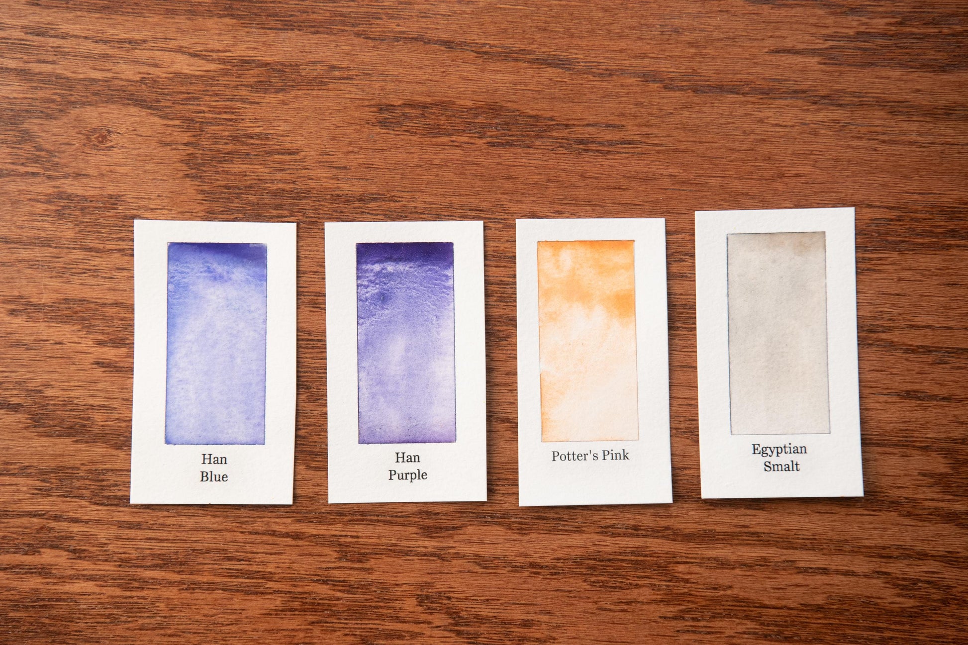 four small rectangular cards with different paint color swatches, arranged on a wooden surface.