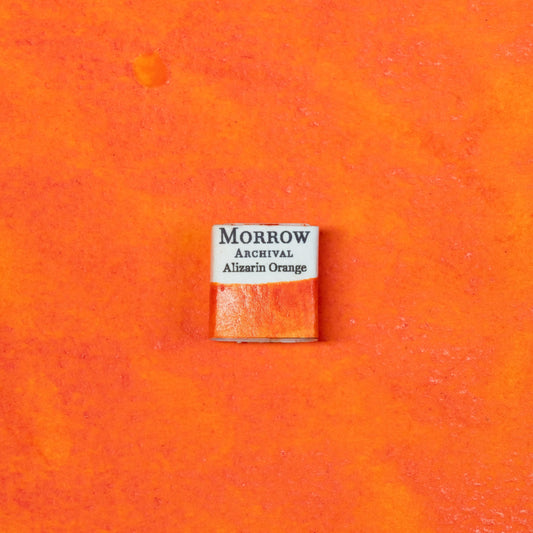 Close-up image of a half pan of Alizarin Orange handmade watercolor paint, showcasing an intensely vibrant, coppery-orange hue with a smooth, glossy surface and deep transparency. The pan rests on a neutral background, emphasizing its bold chroma and artisanal craftsmanship. Ideal for artists seeking a powerful, historically significant orange with unmatched warmth and expressive depth.