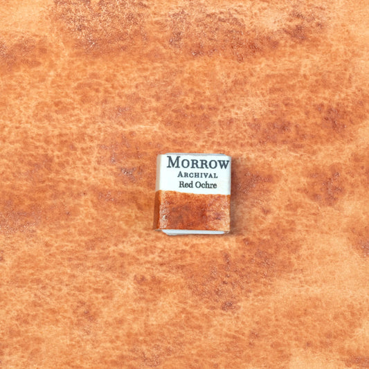 Close-up image of a half pan of Red Ochre handmade watercolor paint, showcasing a rich, earthy red with subtle granulation and a matte finish. The pan is placed on a neutral background, emphasizing its natural mineral composition and artisanal craftsmanship. Perfect for artists seeking a historic, non-toxic pigment with warm, grounded tones.