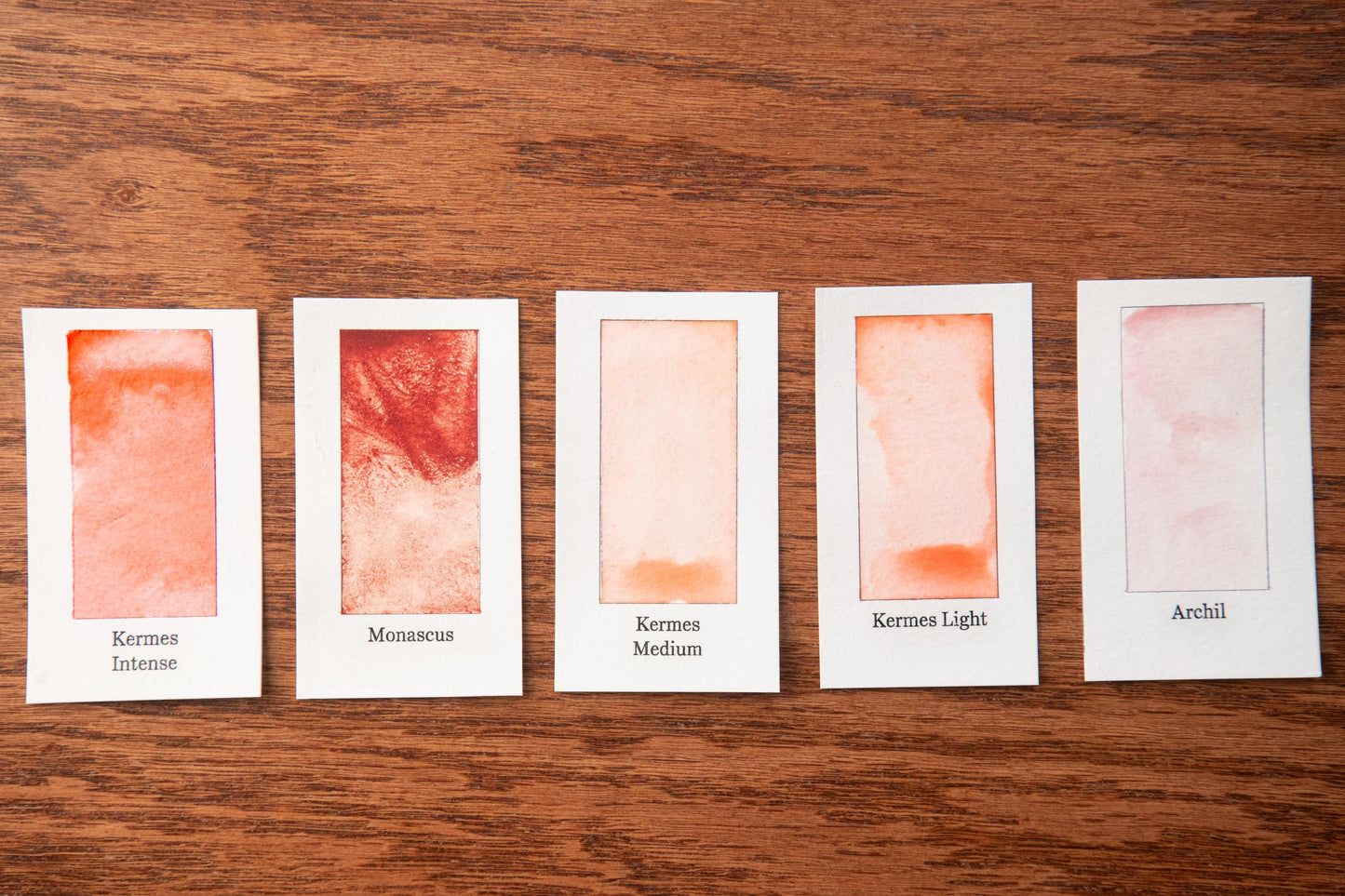 five watercolor paintings with different shades of orange, arranged on a wooden surface.