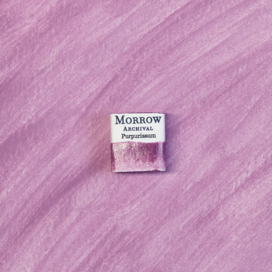 Close-up image of a half pan of Purpurissum handmade watercolor paint, featuring a deep, reddish-purple hue with a smooth, translucent finish and subtle texture. The pan is set on a neutral or ancient-inspired background, emphasizing its origin from Murex sea snails and artisanal craftsmanship. Ideal for artists, collectors, and conservators seeking a true historical pigment of imperial prestige.