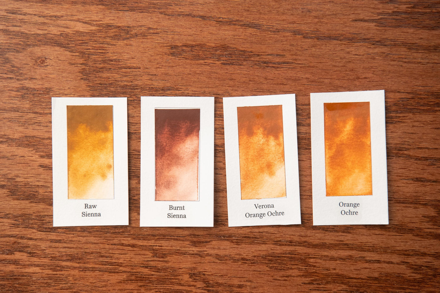 four small cards with different shades of brown, arranged on a wooden surface.