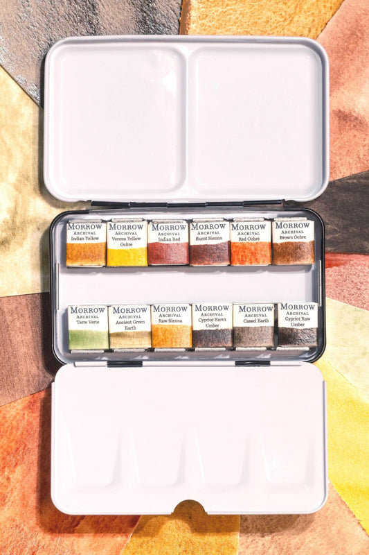 Archival watercolor palette set with 12 handmade pans labeled elegantly, shown with painted swatches behind. Includes Indian Yellow, Verona Yellow Ochre, Indian Red, Burnt Sienna, Red Ochre, Brown Ochre, Terre Verte, Ancient Green Earth, Raw Sienna, Cypriot Burnt Umber, Cassel Earth, and Cypriot Raw Umber. Rich earth tones crafted with honey and gum arabic, ideal for classical, portrait, and landscape work.