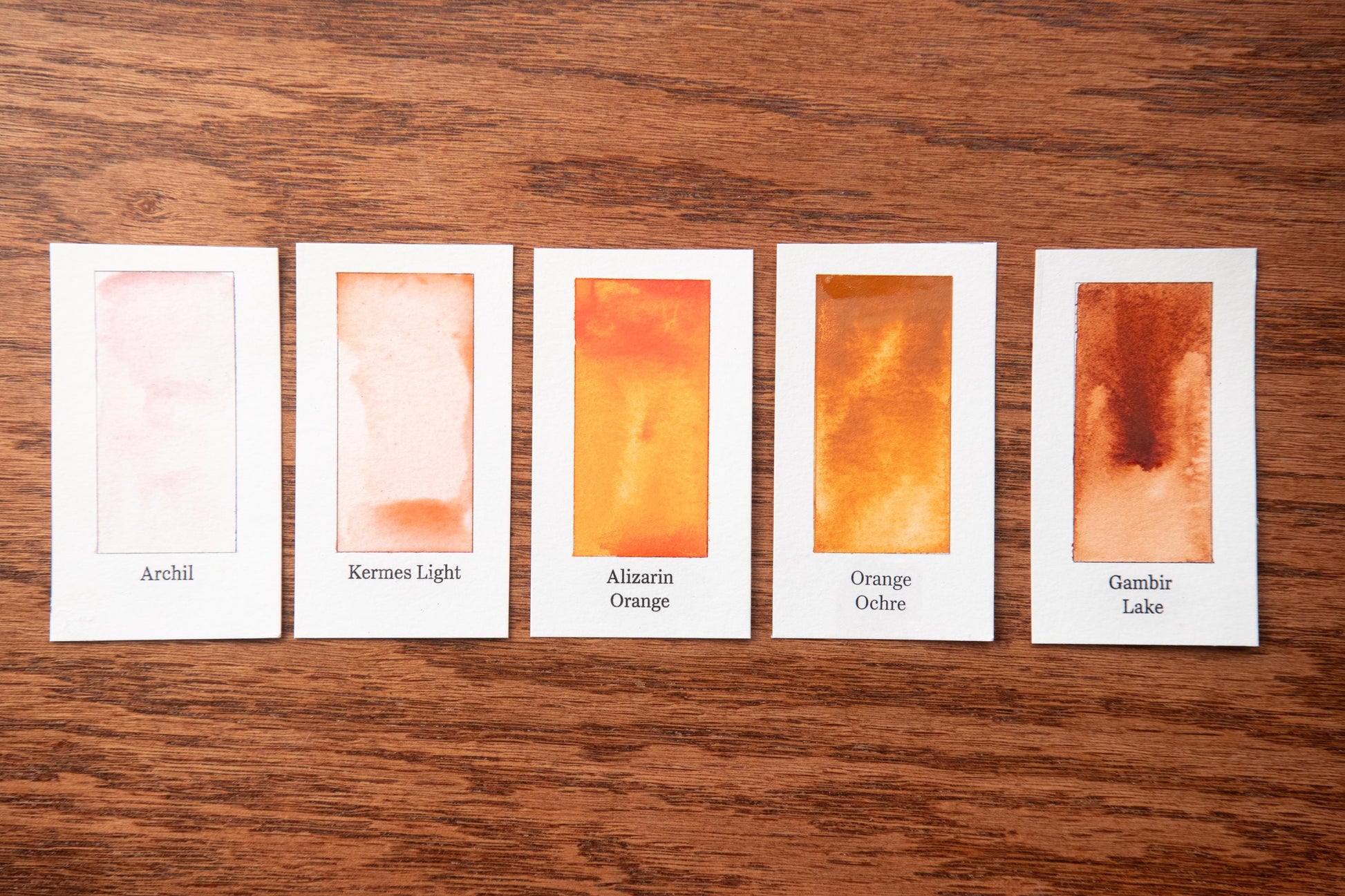 five watercolor paintings with different color shades, arranged on a wooden surface.