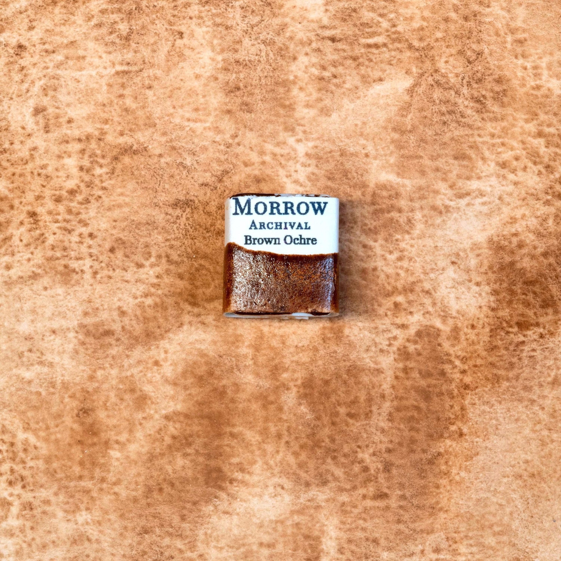 Close-up image of a half pan of Brown Ochre handmade watercolor paint, showing a warm, muted brown with subtle granulation and a soft matte finish. The pan is set against a neutral background, highlighting its natural earth origin and artisanal, small-batch craftsmanship. Ideal for artists looking for a classic, non-toxic brown pigment with historical roots and a grounded, organic feel.