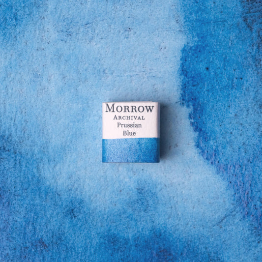 Handmade Prussian Blue natural watercolor paint half pan shown on a textured watercolor painting. Created from pure single-pigment iron ferrocyanide, this historic deep blue offers rich opacity, strong staining power, and beautiful granulation‚Äîperfect for landscape painting, botanical art, and classical illustration. A beloved eco-friendly gift for watercolor artists and collectors seeking small-batch, archival-quality, all-natural handmade pigments with centuries of artistic legacy.