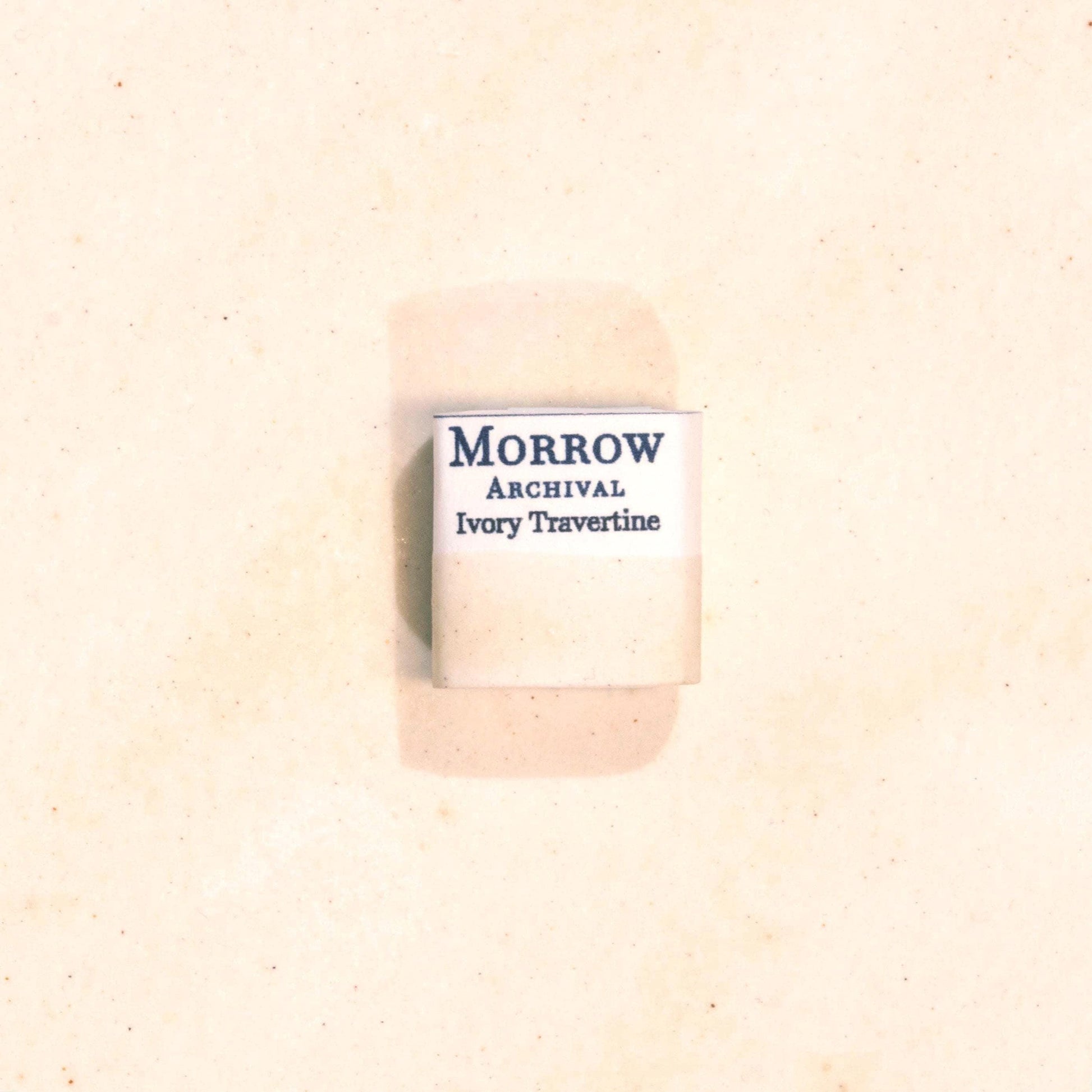 Handmade Ivory Travertine natural watercolor paint half pan resting on a textured watercolor painting. Made from pure single-pigment natural stone, this soft, warm off-white offers subtle granulation and delicate transparency, perfect for botanical painting, historical artwork, and fine art layering. A beautiful eco-friendly gift for watercolor artists and collectors seeking small-batch, archival-quality, all-natural handmade pigments inspired by ancient materials.