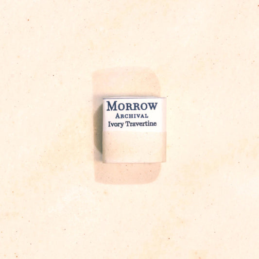 Handmade Ivory Travertine natural watercolor paint half pan resting on a textured watercolor painting. Made from pure single-pigment natural stone, this soft, warm off-white offers subtle granulation and delicate transparency, perfect for botanical painting, historical artwork, and fine art layering. A beautiful eco-friendly gift for watercolor artists and collectors seeking small-batch, archival-quality, all-natural handmade pigments inspired by ancient materials.