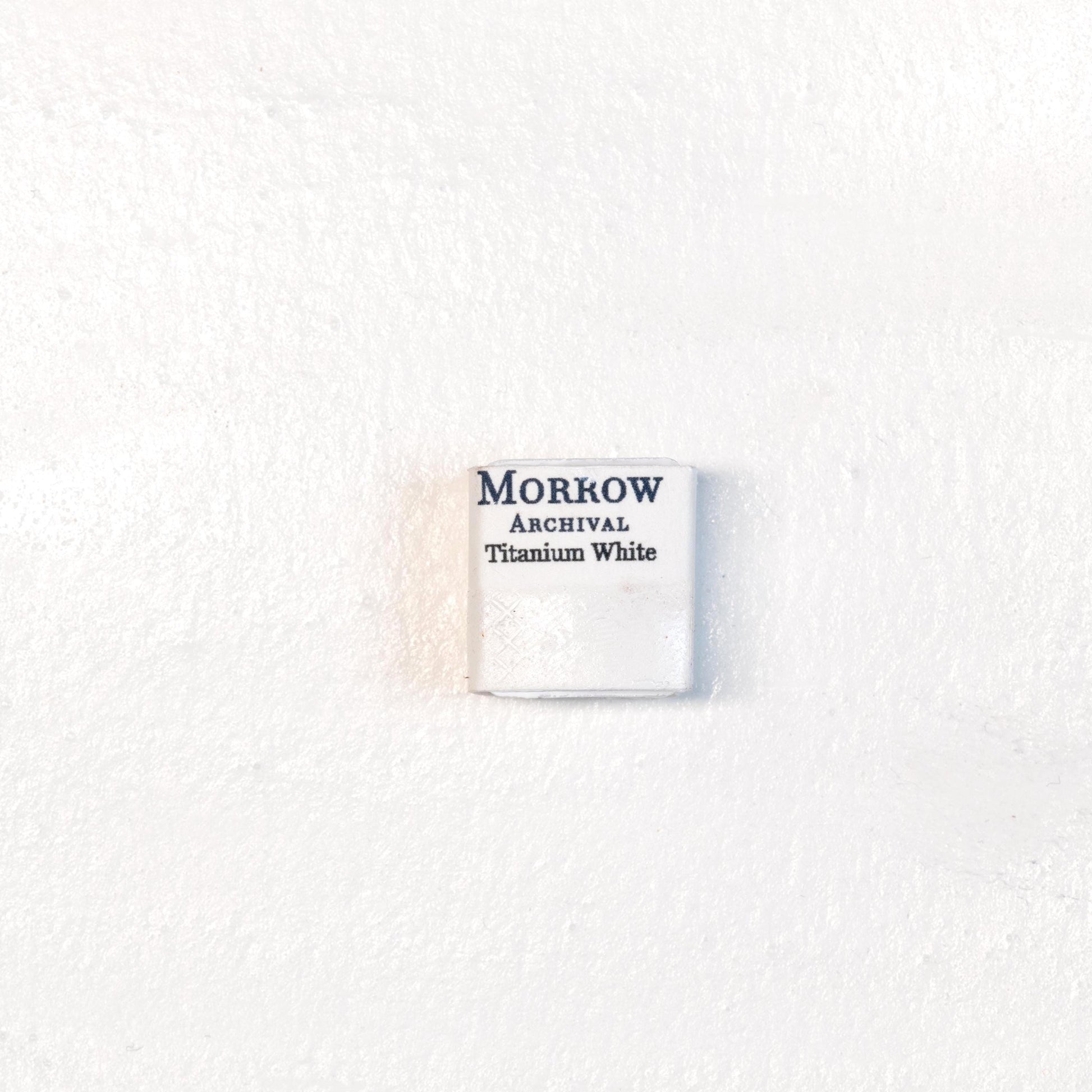 Close-up image of a half pan of Titanium White handmade watercolor paint, showing a bright, pure white with a smooth, opaque matte surface. The pan rests on a neutral background, highlighting its mineral purity and artisanal craftsmanship. Ideal for artists seeking a clean, permanent white for highlights, tints, and opaque effects.