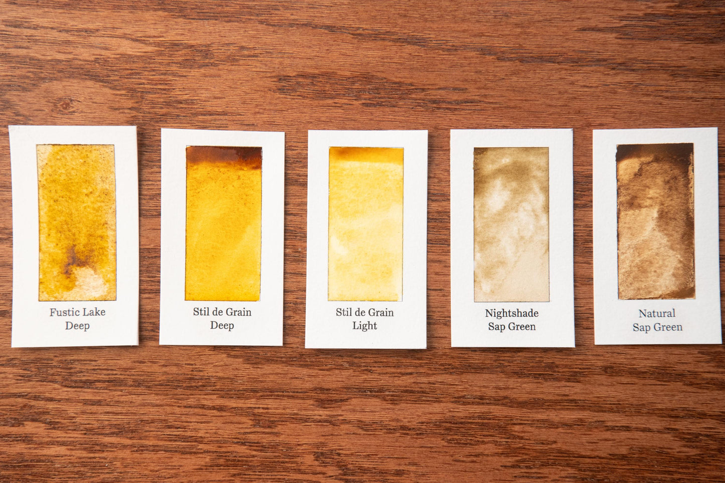 five different shades of yellow paint, each labeled with a different description, arranged on a wooden surface.