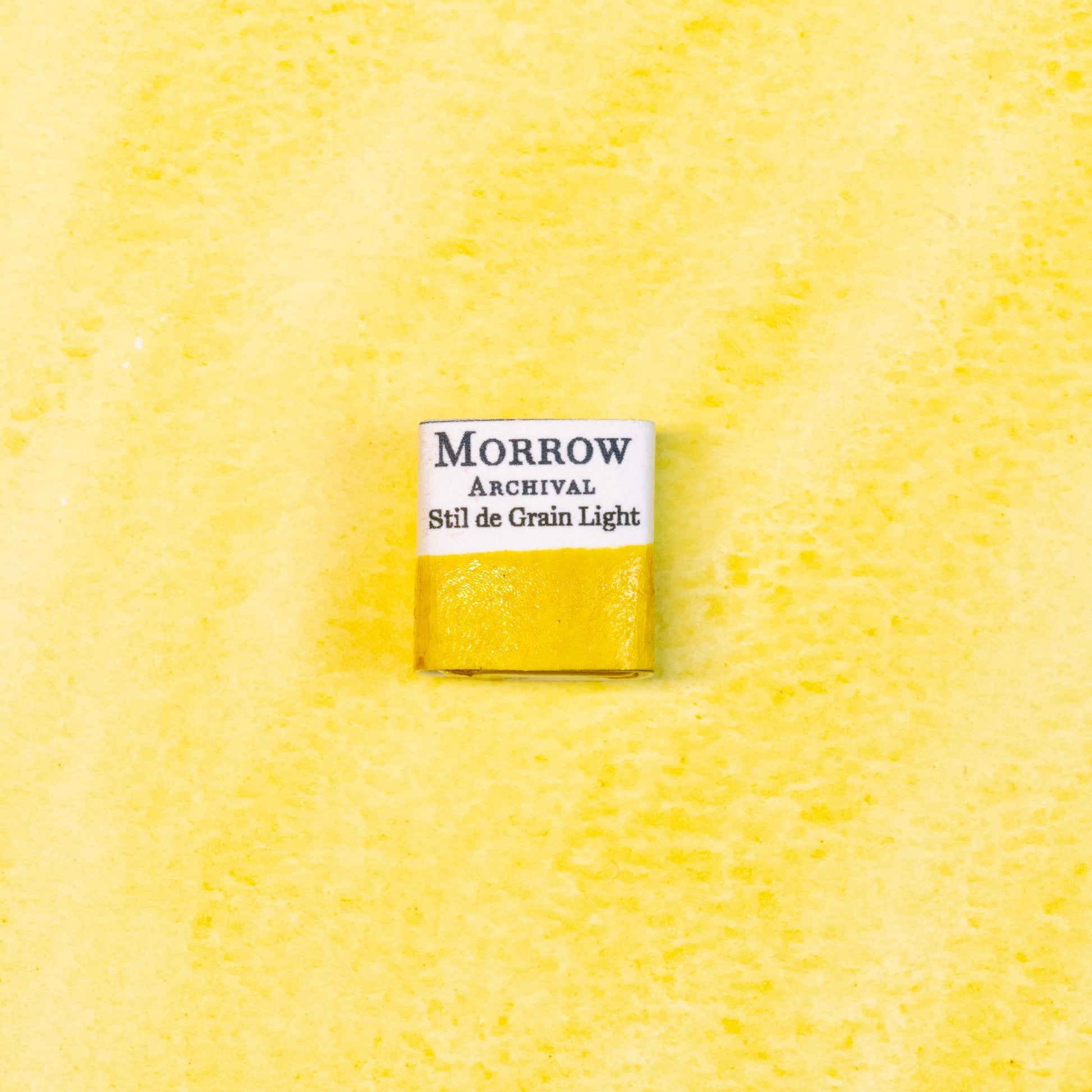 Close-up image of a half pan of Stil de Grain Light (Buckthorn Lake) handmade watercolor paint, showing a pale golden-yellow hue with soft, translucent texture. The pan rests on a neutral background, highlighting the botanical origin and traditional craftsmanship. Ideal for artists seeking a luminous, historic plant-based yellow with gentle warmth and natural charm.