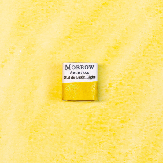 Close-up image of a half pan of Stil de Grain Light (Buckthorn Lake) handmade watercolor paint, showing a pale golden-yellow hue with soft, translucent texture. The pan rests on a neutral background, highlighting the botanical origin and traditional craftsmanship. Ideal for artists seeking a luminous, historic plant-based yellow with gentle warmth and natural charm.