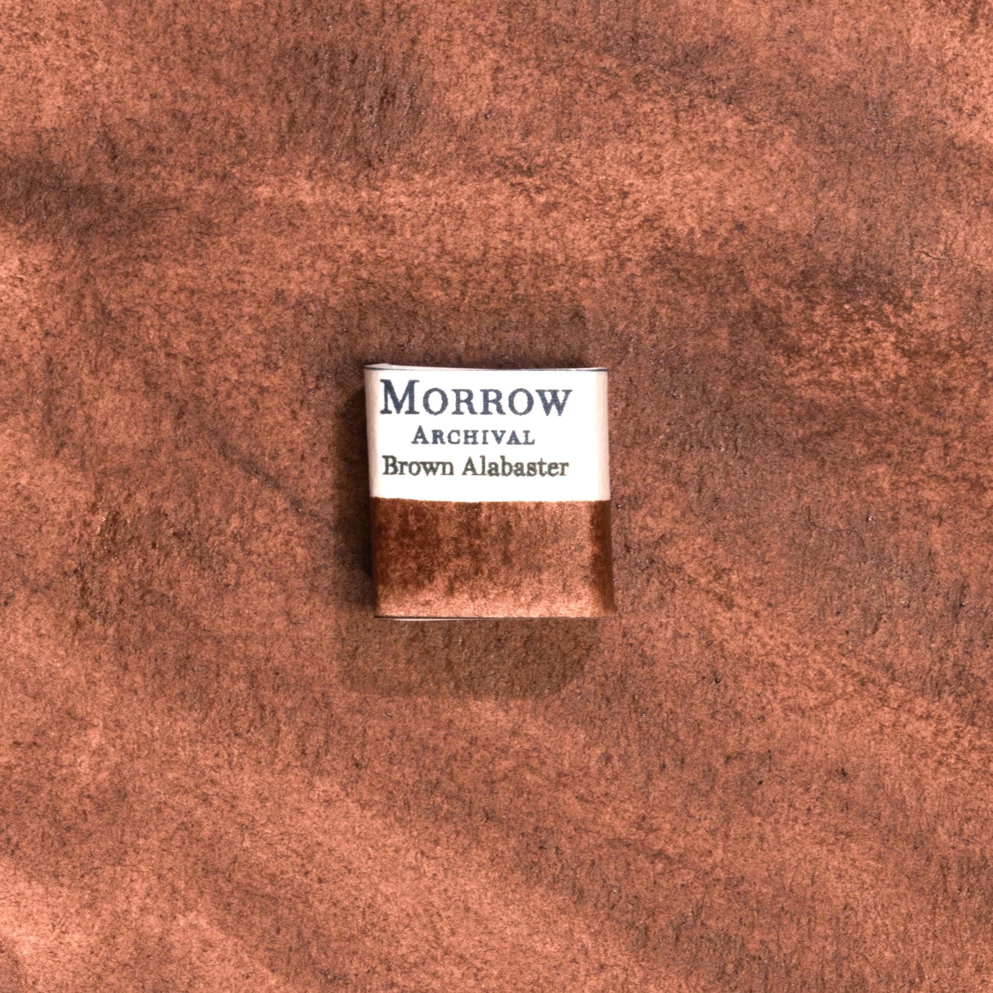 Handmade Brown Alabaster natural watercolor paint half pan resting on a textured watercolor painting. Crafted from pure single-pigment natural stone, this warm, earthy brown offers soft granulation and gentle transparency, ideal for botanical illustration, landscape painting, and historical artwork. A perfect eco-friendly gift for watercolor artists, nature lovers, and collectors seeking small-batch, archival-quality, all-natural handmade pigments inspired by ancient materials.