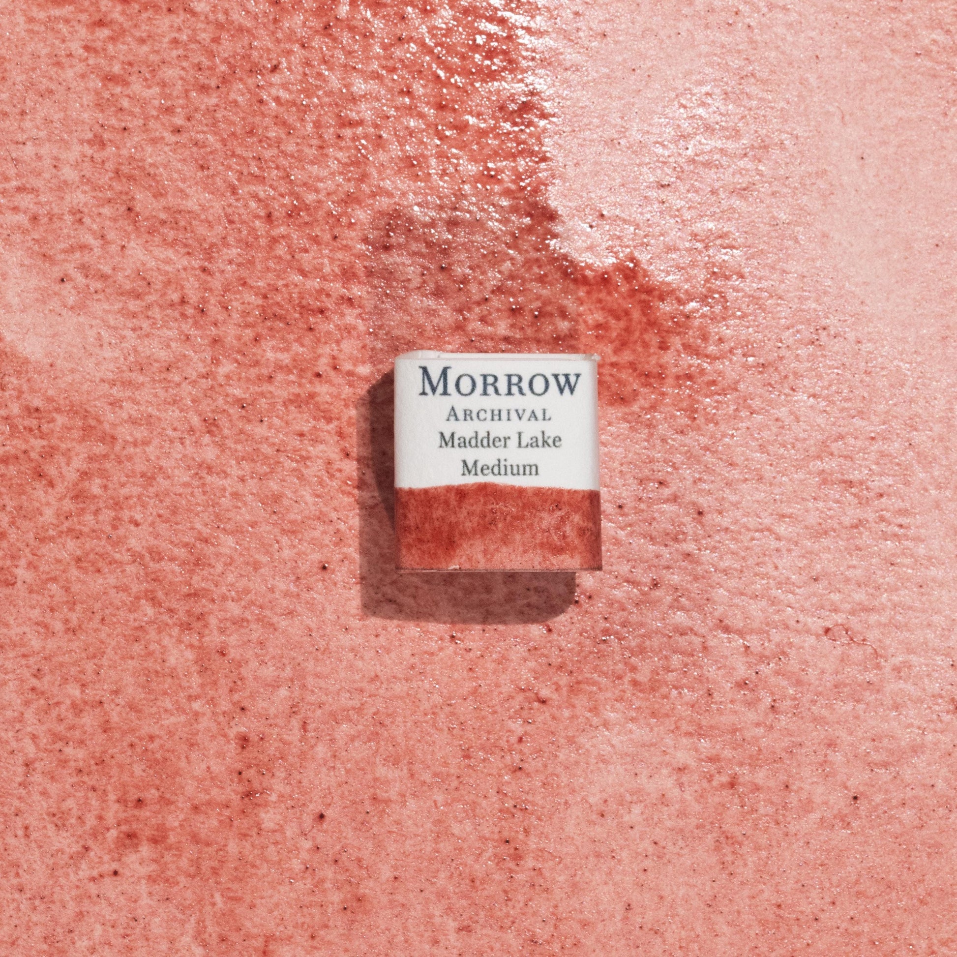 Handmade Madder Lake Medium natural watercolor paint half pan resting on a textured watercolor painting. Made from pure single-pigment laked madder root, this deep rose-red hue offers rich transparency and soft granulation, ideal for botanical art, historical painting, and portrait work. A beautiful eco-friendly gift for watercolor artists and collectors seeking small-batch, archival-quality, all-natural handmade pigments with centuries of artistic heritage.