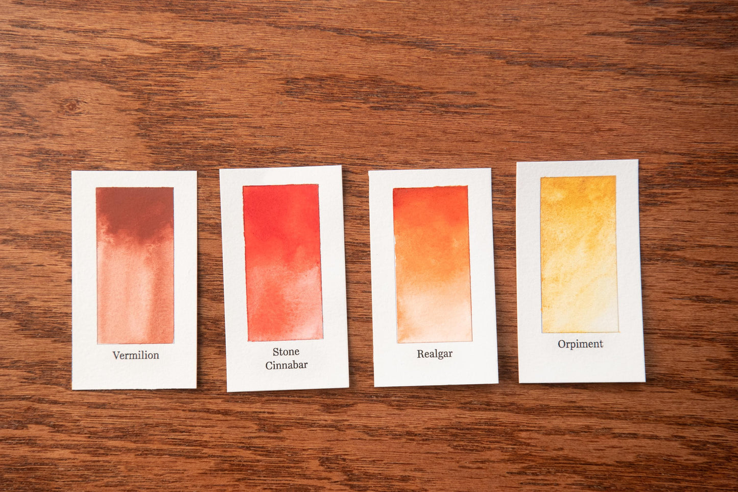 four color swatches arranged on a wooden surface, each swatch representing a different shade of orange.