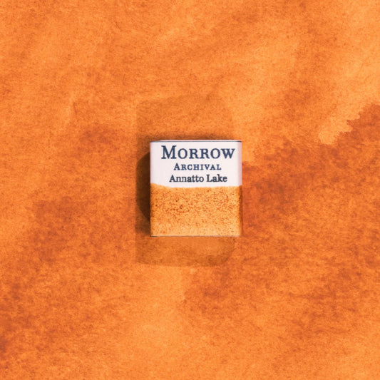 Handmade Annatto Lake Orange natural watercolor paint half pan shown on a textured watercolor painting. Created from pure single-pigment annatto seeds, this warm, glowing orange offers beautiful transparency and soft granulation, ideal for botanical art, historical painting, and fine art illustration. A perfect eco-friendly gift for watercolor artists, nature lovers, and collectors seeking small-batch, archival-quality, all-natural handmade pigments.