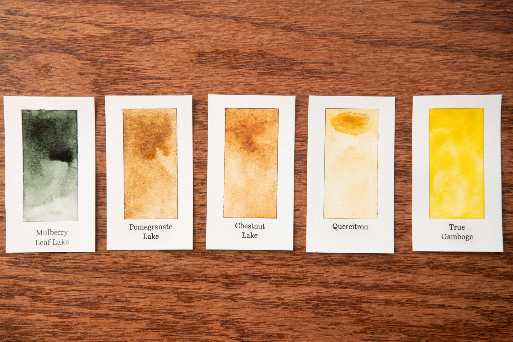 five watercolor paintings on a wooden surface, each with a different color and texture.